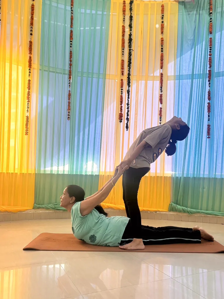 Bhumika Pathak guiding a student through a supported backbend during a class